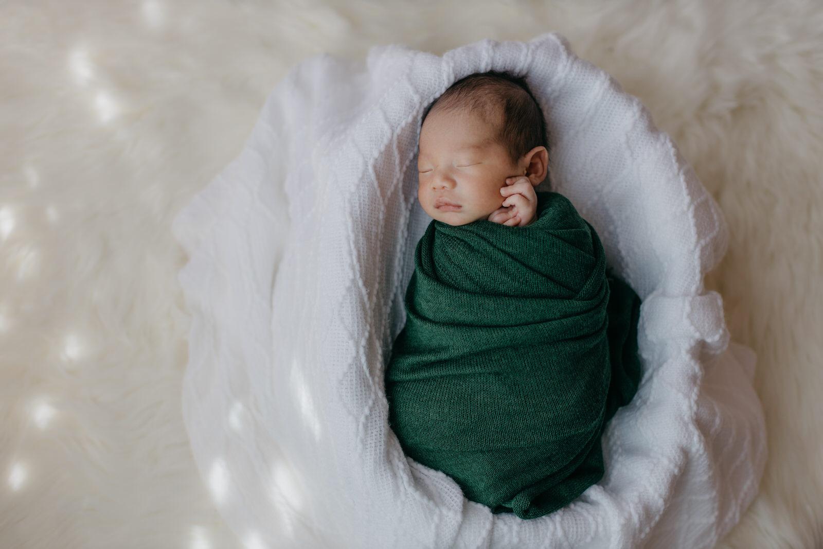 Newborn photography Kuala Lumpur a baby wrapping with green cloth in a busket.