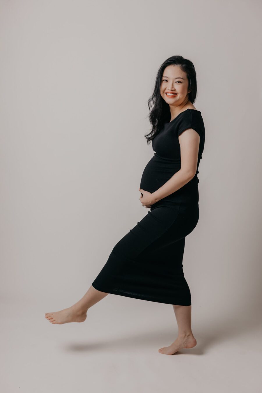 Mini Maternity Photo Session - Expectant mother and father posing in minimalist style against creamy beige backdrop at Darkroom Project Studio in Pinnacle Kelana Jaya, Kuala Lumpur.