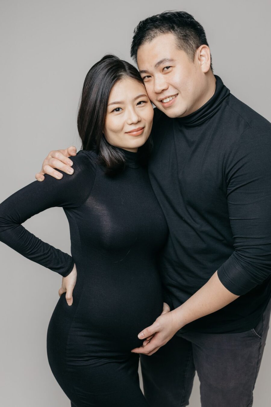 Mother and father embracing, smiling at the camera during a maternity photo session.