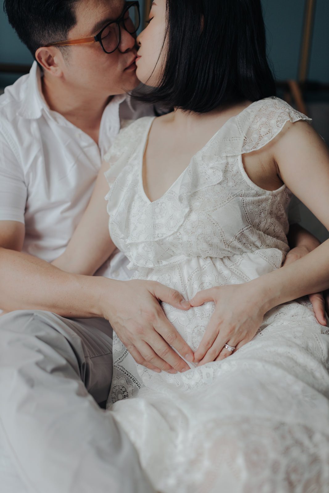 Expecting Parents Kissing: Husband and expecting wife sharing a kiss while husband's hands form a heart shape over wife's pregnant belly.