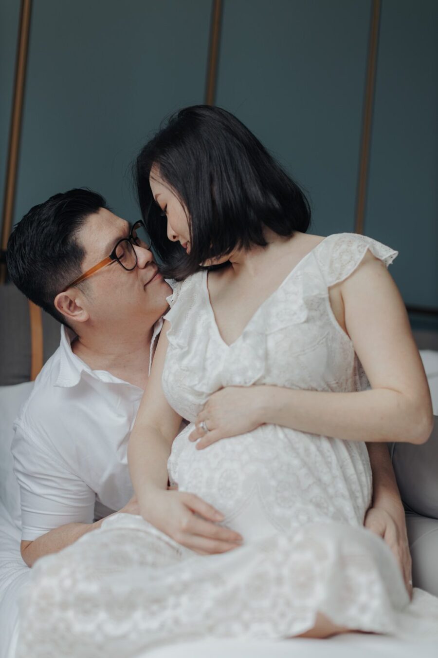 Tender Moment with Expecting Parents: KimSun and Rachel sharing an intimate moment on the bed, with KimSun gently holding Rachel's baby bump.