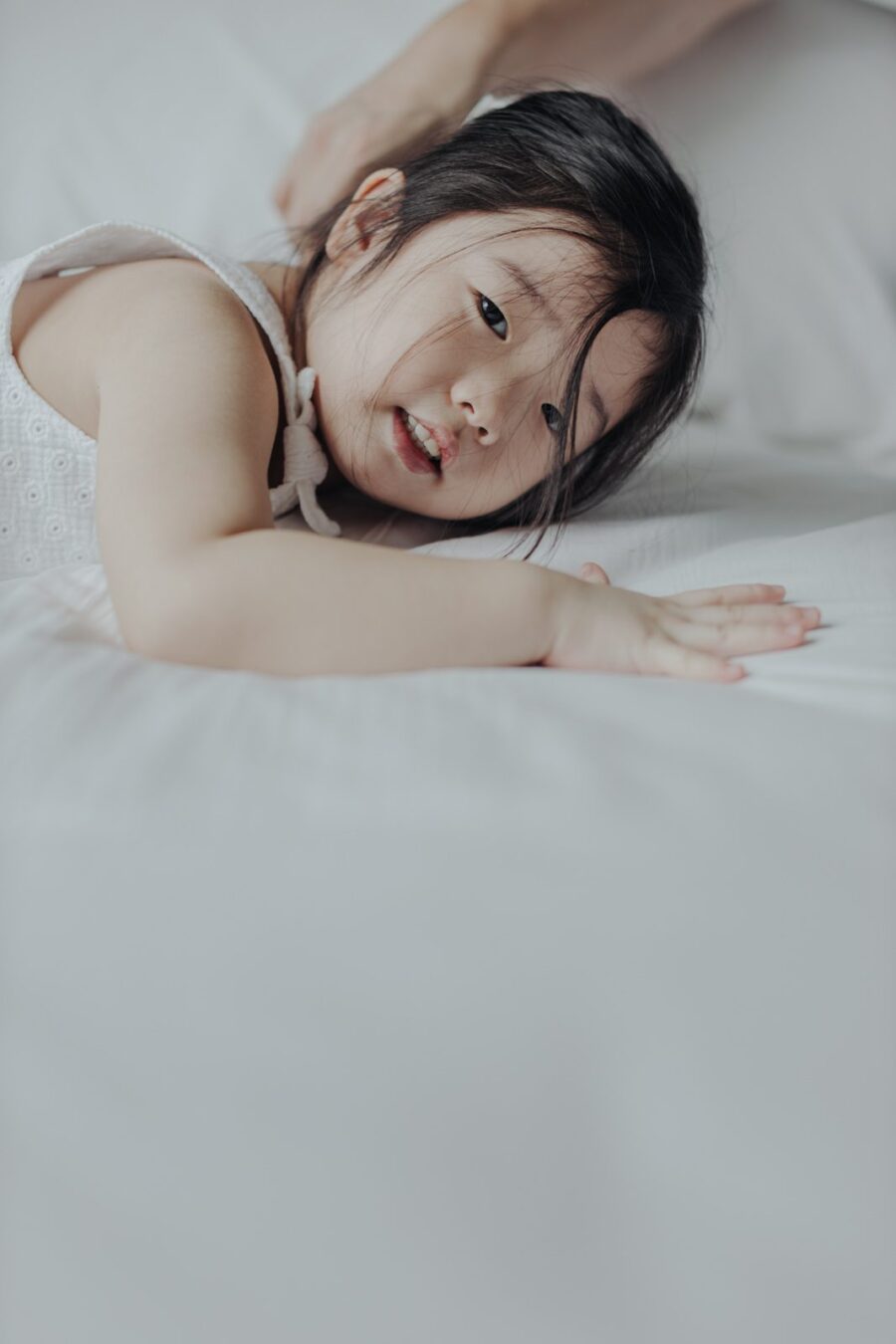 Little Girl on the Bed: Close-up of Naomi lying on a bed, looking playfully at the camera with a relaxed expression.