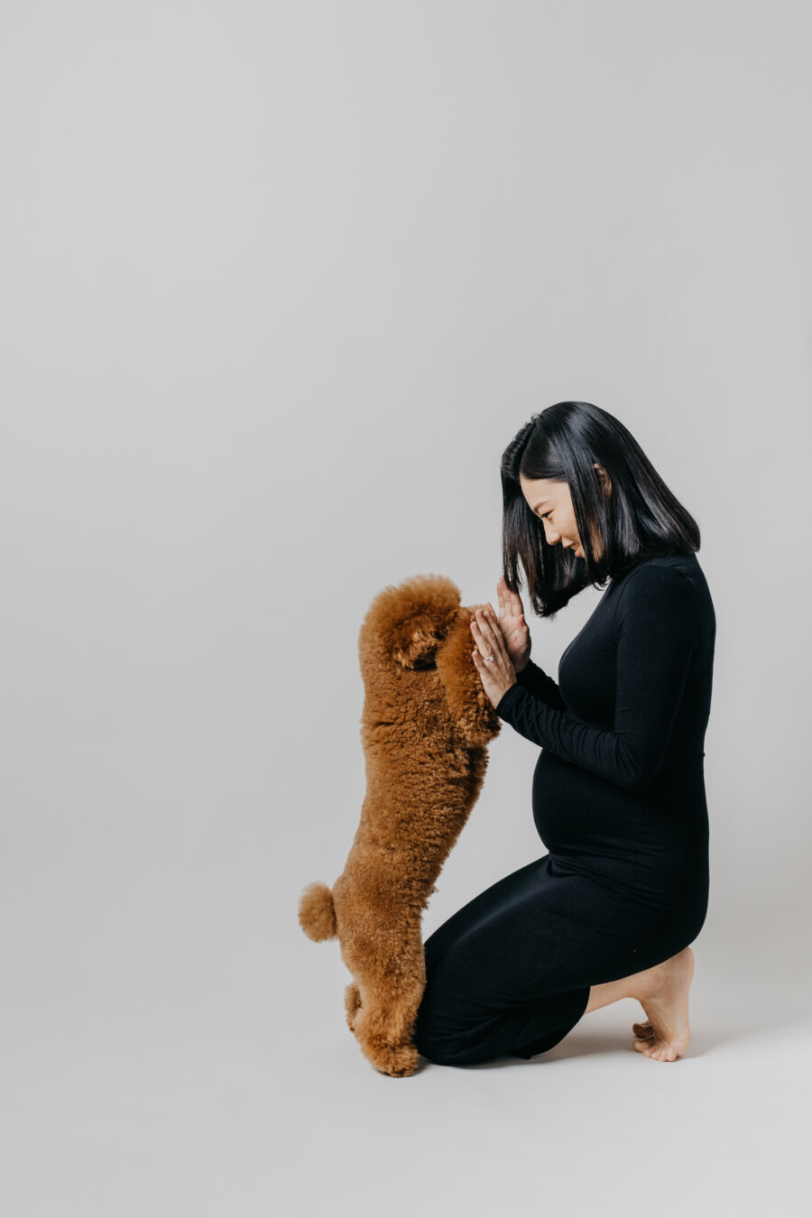 Mother kneeling and playing with their poodle, Milo, during a maternity photo session