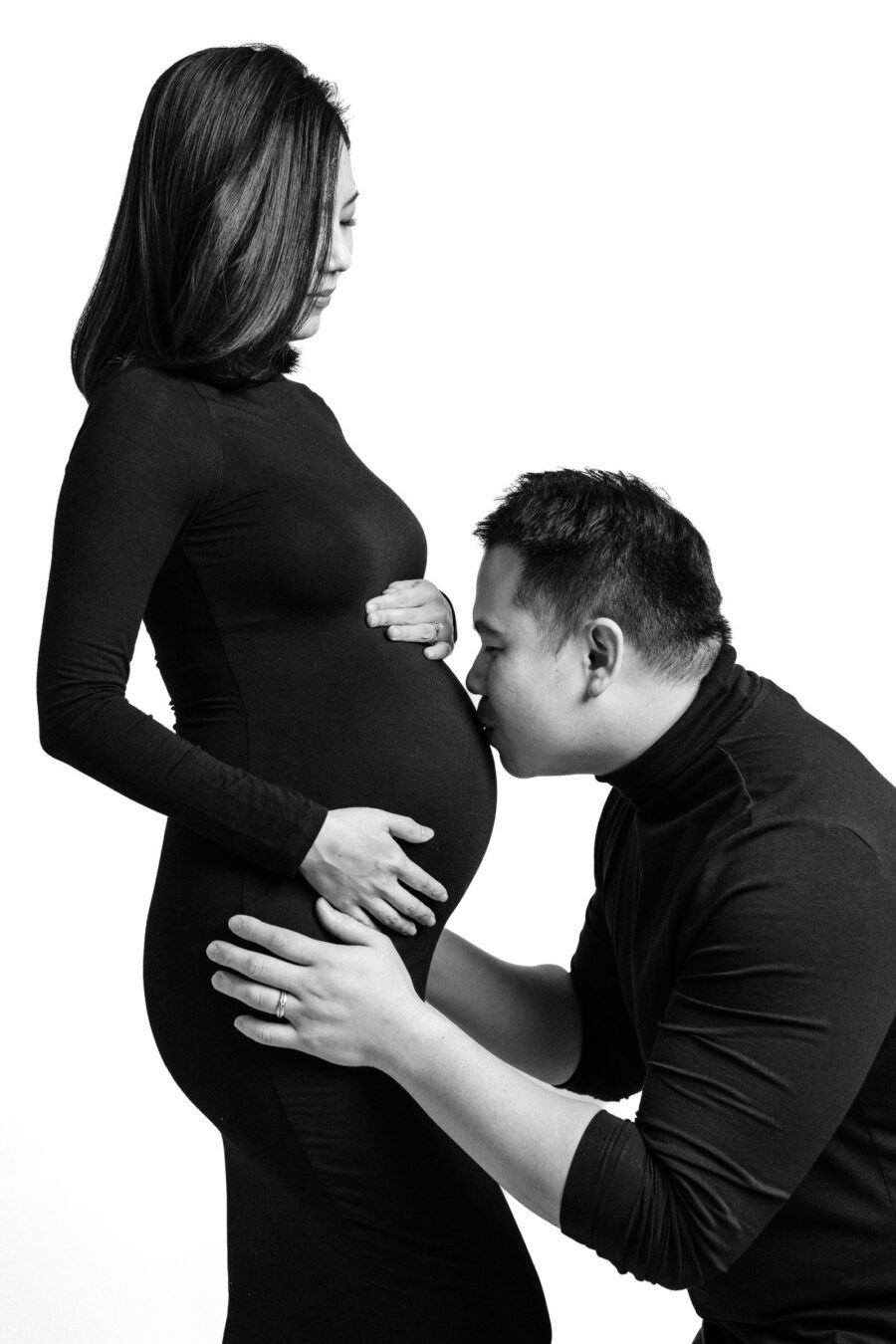 Father kneeling and hugging mother's baby bump during a maternity photo session.