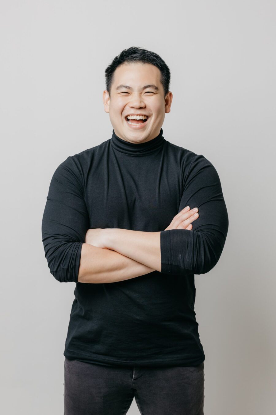 Father smiling with arms crossed in a black sweater during a maternity photo session.