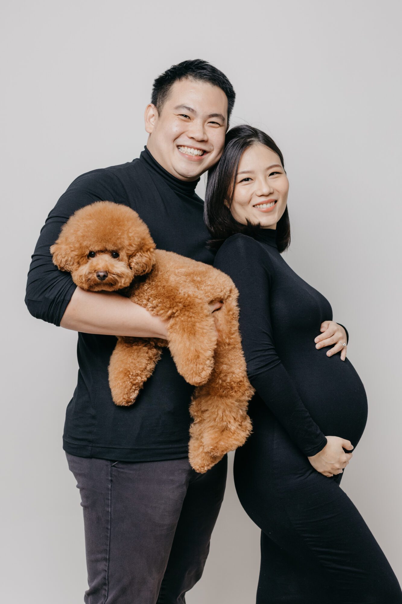 Mother and father embracing, smiling at the camera during a maternity photo session.