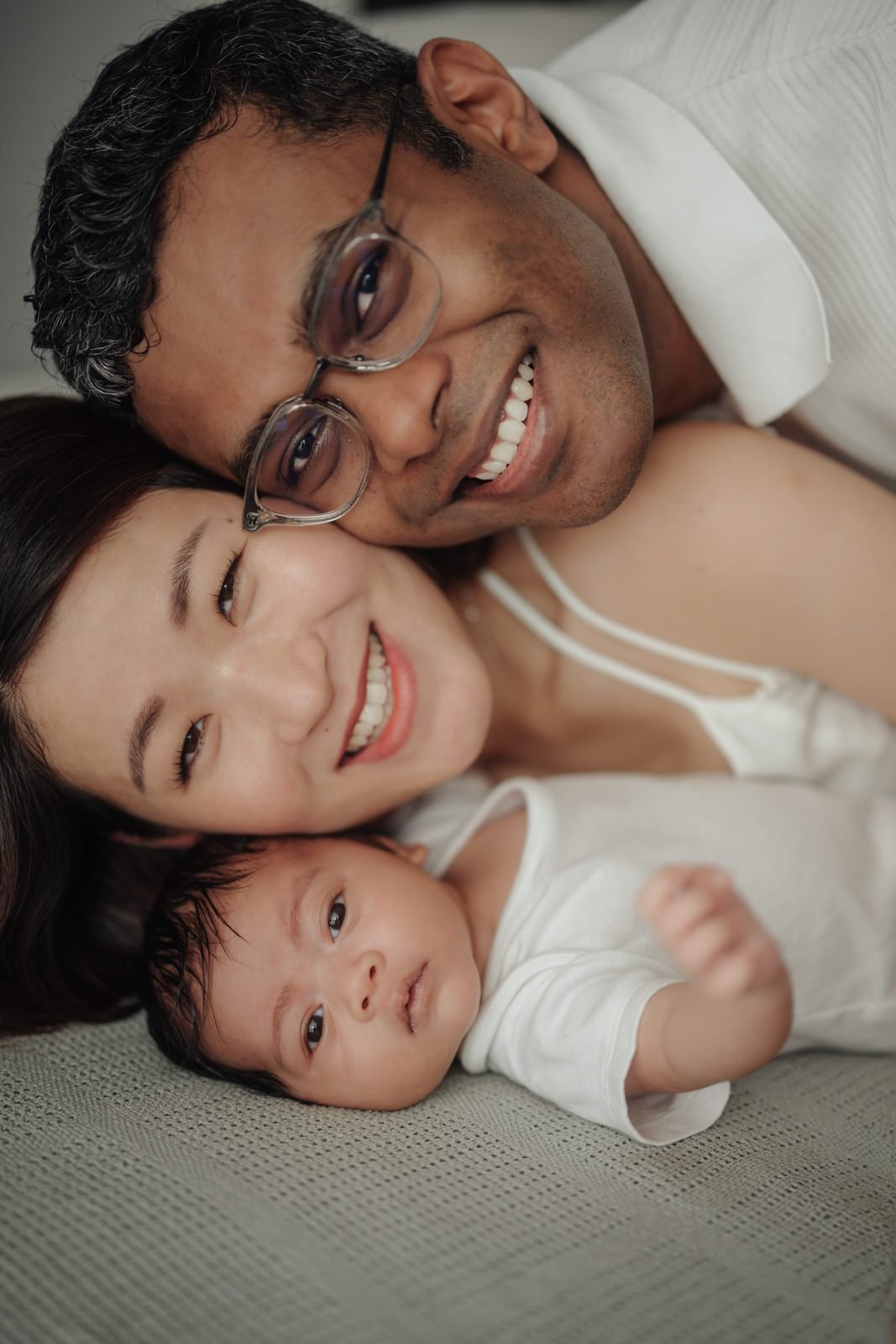 Mother and Father cuddling Cleo together, showcasing a warm baby portrait that encapsulates genuine affection in a portrait at home session. Cliff Choong Photography