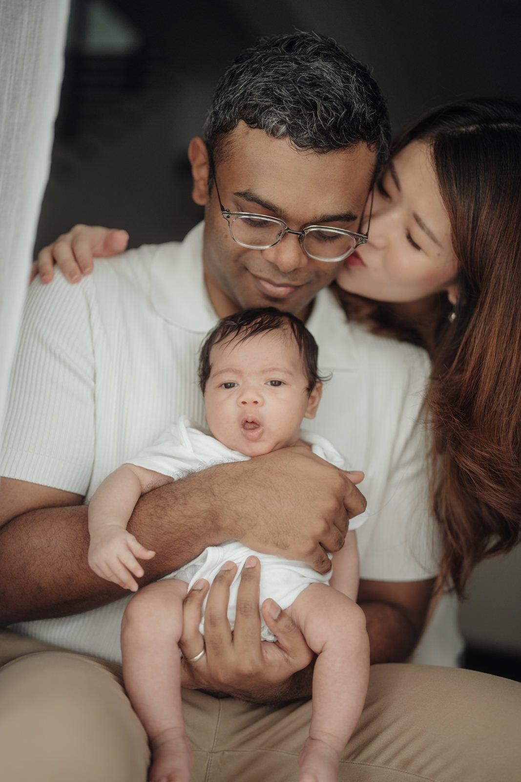 Parents holding baby Cleo between them, portraying a timeless baby portrait enriched by the comfort of a portrait at home session. Cliff Choong Photography.